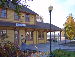 Historic Roseville train station building with trees and a railroad track in the background.